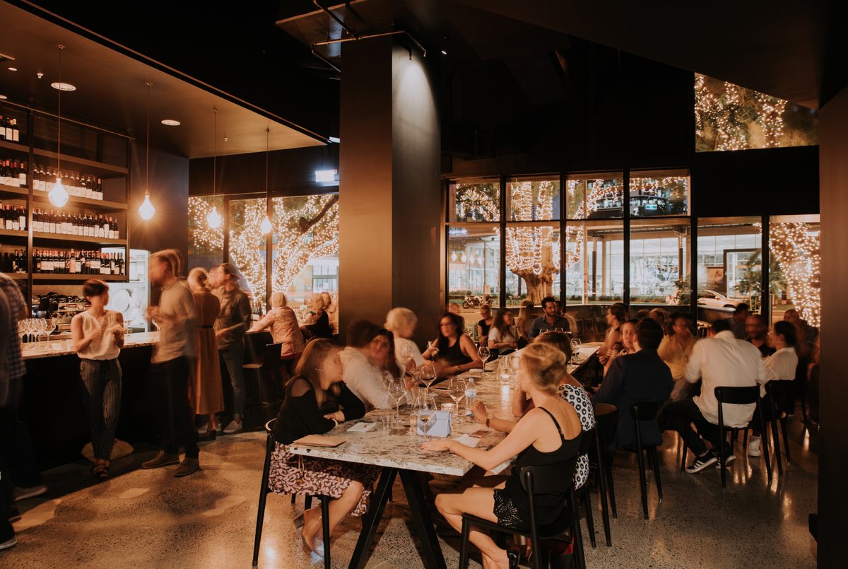 Snack Man's dark, moody dining room with communal tables, pendant lights and a wine wall